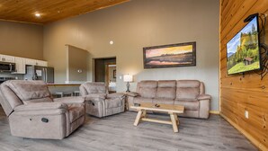 A living room with a sofa, a recliner, and a coffee table. There is a kitchen in the background with a microwave and refrigerator.