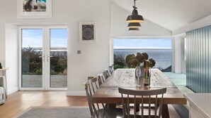Un coin repas avec une table et des chaises en bois, un luminaire suspendu et une vue sur la mer grâce à de grandes fenêtres.