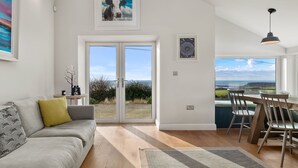 Un vaste espace de vie comprenant un canapé, une table à manger avec des chaises et une vue sur l’extérieur grâce à de grandes portes vitrées.