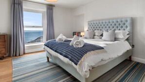 Une chambre avec un grand lit, une vue sur la mer et une commode en bois.