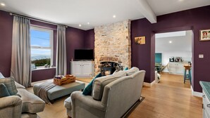 Un salon avec une cheminée en pierre, un canapé, un téléviseur et une vue sur la mer.