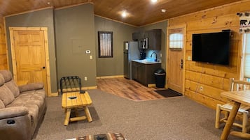 A cozy cabin interior with a sofa, a small table, a television, and a kitchenette.