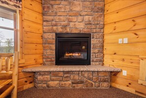 A fireplace with a stone surround, wooden walls, and a carpeted floor.