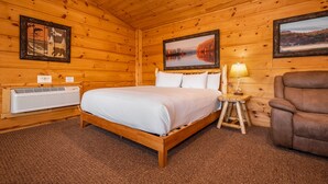 A wooden cabin bedroom with a bed, a chair, a lamp, and two framed pictures on the walls.
