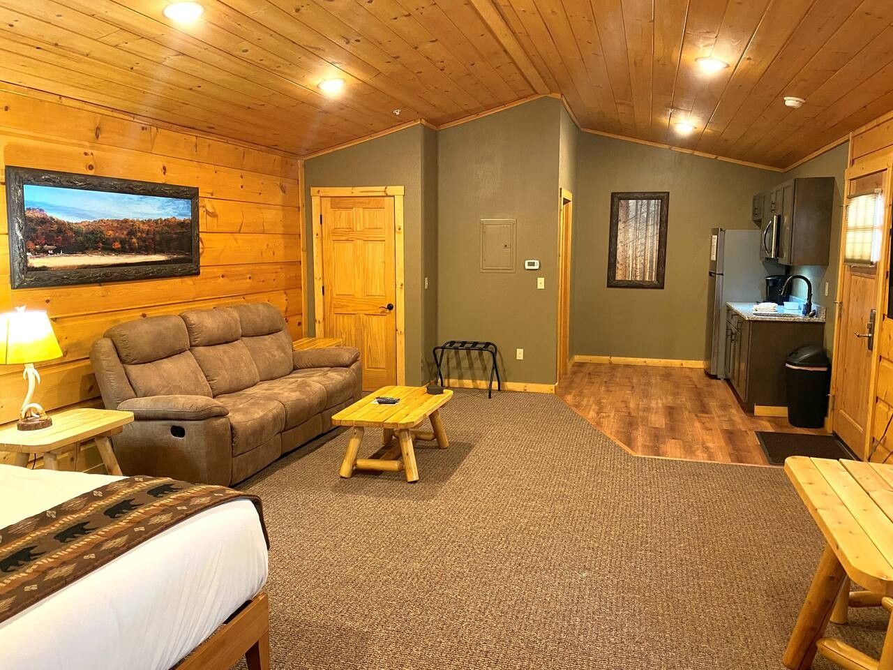 A cozy cabin interior with a sofa, a small wooden table, a bed, a dining table, and a kitchen area.