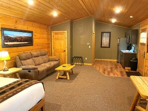A cozy cabin interior with a sofa, a small wooden table, a bed, a dining table, and a kitchen area.