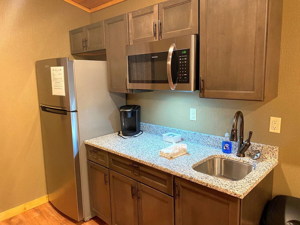 A compact kitchen with a refrigerator, microwave, coffee maker, and a sink with a faucet.