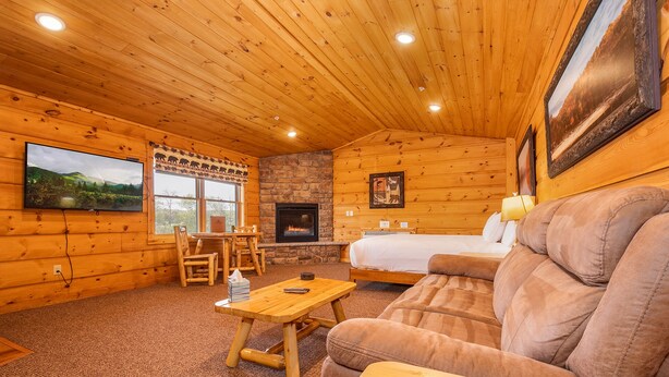 A log cabin interior with a fireplace, a television, a sofa, and a dining area.