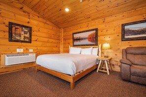 A wooden cabin room with a bed, a chair, a nightstand, and two framed pictures on the walls.