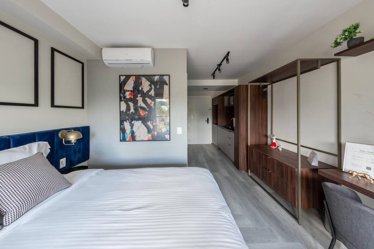 A modern hotel room with a bed, a desk, and a kitchenette.