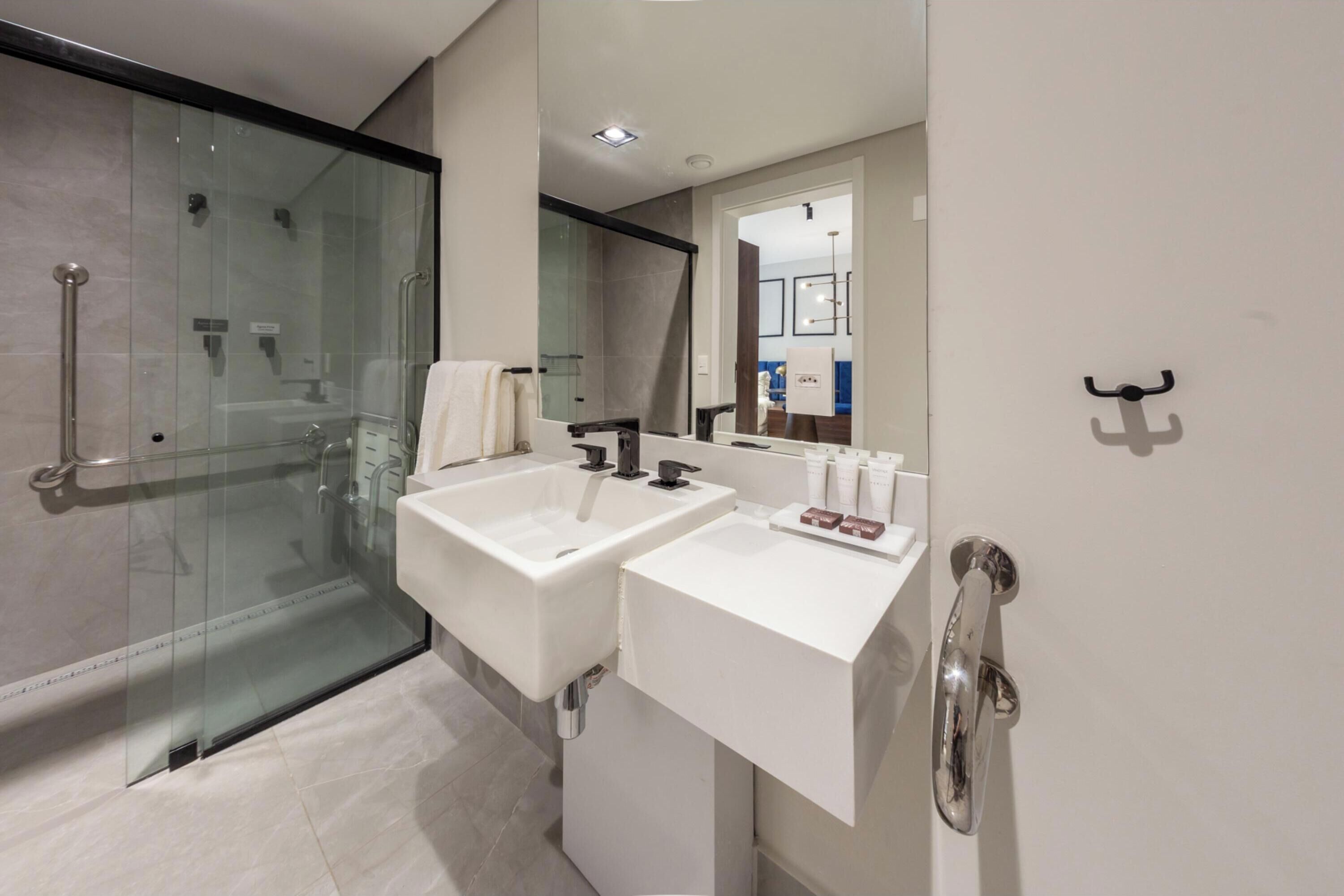 Un baño moderno con ducha de vidrio, dos lavamanos blancos y un espejo grande.