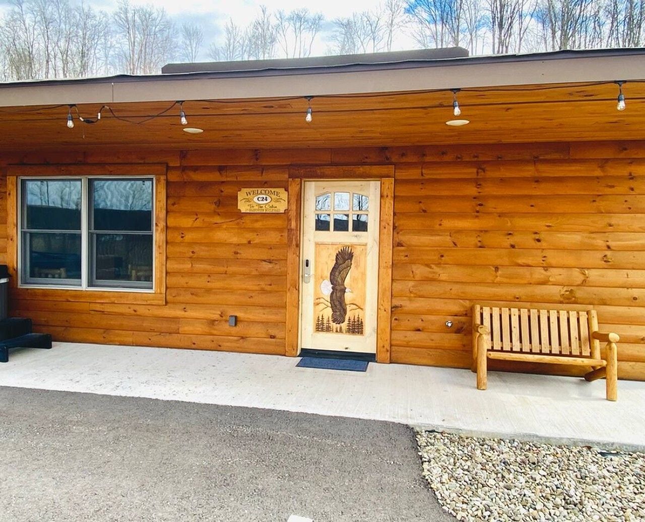 A wooden cabin with a welcome sign, a bench, and a door with an eagle design.