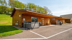 A wooden cabin with a covered patio area, a grill, and a hot tub. - Grandview Cabin Suite 24-Hot Tub (McHenry)