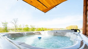 A hot tub with a wooden roof, surrounded by greenery and a clear sky. - Grandview Cabin Suite 24-Hot Tub (McHenry)