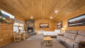 A cozy cabin interior with a stone fireplace, wooden walls, a bed, a sofa, and a dining area. - Grandview Cabin Suite 27-Hot Tub, Dog Friendly (McHenry)