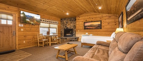 A log cabin interior with a stone fireplace, wooden furniture, and a bed.