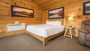 A wooden cabin room with a bed, a chair, and two framed pictures on the walls. - Grandview Cabin Suite 27-Hot Tub, Dog Friendly (McHenry)