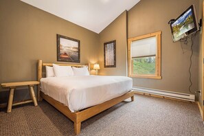 A bedroom with a large bed, a bedside table, a wall-mounted TV, and two framed pictures.