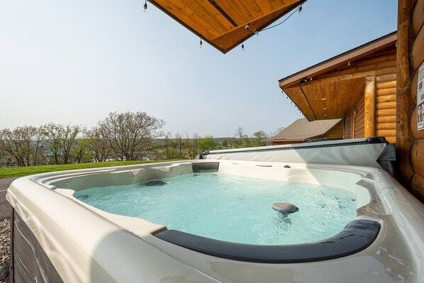 A hot tub with a wooden deck and a view of trees and hills.