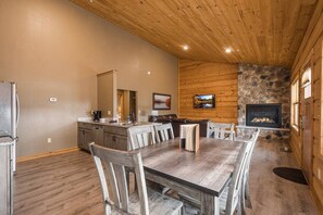 A spacious dining area with a wooden table and chairs, a kitchen with a stone accent wall, and a fireplace.