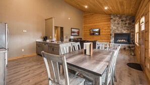Un comedor amplio con una mesa y sillas de madera, una cocina con refrigerador y estufa, y una chimenea de piedra.