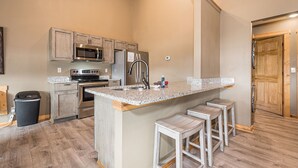 Una cocina con gabinetes de madera, electrodomésticos de acero inoxidable, encimera de granito y una zona con taburetes de bar.