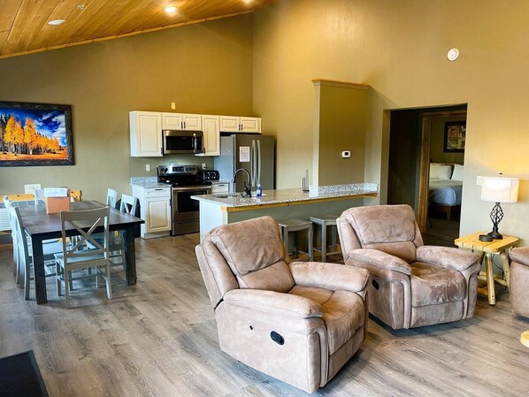 A modern living room with a dining area, a kitchen, and a large window.