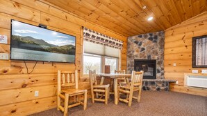 A cozy cabin interior with a stone fireplace, wooden walls, a large TV, and a dining area with wooden chairs. - Grandview Cabin Suite 29-Full Kitchen (McHenry)