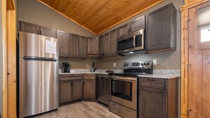 A modern kitchen with stainless steel appliances, dark wooden cabinets, and a granite countertop. - Grandview Cabin Suite 29-Full Kitchen (McHenry)