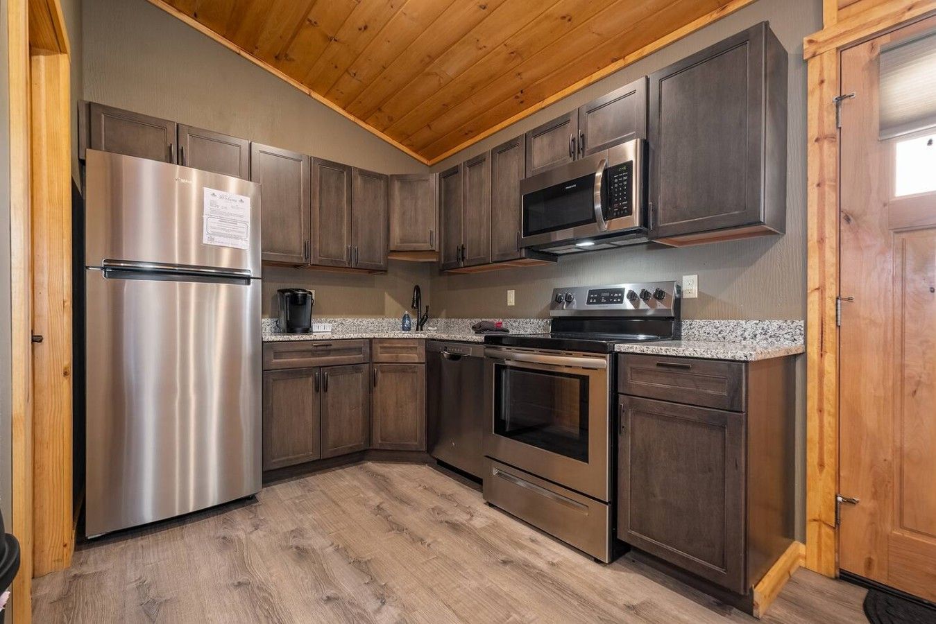 A compact kitchen with a stainless steel refrigerator, a microwave, an oven, and a coffee maker.