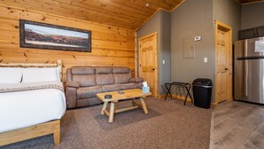 A cozy room with a bed, a sofa, a small table, a trash bin, and a refrigerator. - Grandview Cabin Suite 29-Full Kitchen (McHenry)