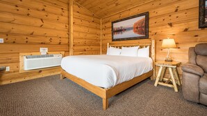 A wooden cabin bedroom with a bed, a nightstand with a lamp, and a framed picture on the wall. - Grandview Cabin Suite 30-Hot Tub, Dog Friendly (McHenry)