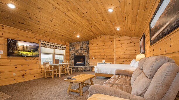 A cozy log cabin interior with a stone fireplace, wooden furniture, and a television mounted on the wall. - Grandview Cabin Suite 30-Hot Tub, Dog Friendly (McHenry)