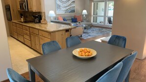 A modern kitchen with wooden cabinets and a granite countertop, a dining area with a table and blue chairs, and a living room with a sofa and a coffee table. - Bright Sedona Retreat with Castle Rock Views (Sedona)