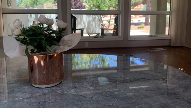 A room with a marble floor, large windows, and a copper vase with white roses. - Bright Sedona Retreat with Castle Rock Views (Sedona)