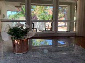 A room with a marble floor, large windows, and a copper vase with white roses. - Bright Sedona Retreat with Castle Rock Views (Sedona)