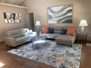 A living room with a sectional sofa, a coffee table, two lamps, a rug, and abstract wall art.
