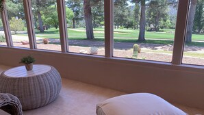 A room with a large window overlooking a golf course, wicker furniture, and a small potted plant. - Bright Sedona Retreat with Castle Rock Views (Sedona)