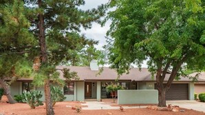 A single-story house with a front porch, a garage, and a small front yard with a cactus and a tree. - Bright Sedona Retreat with Castle Rock Views (Sedona)