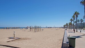 Una playa con un paseo marítimo de madera, palmeras y sombrillas de playa.