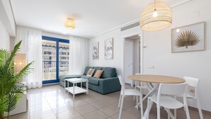 Una sala de estar moderna con un sofá verde, sillas blancas, una mesa de comedor de madera y un ventanal con contraventanas azules.