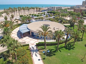 A circular building with a blue roof, surrounded by palm trees and a beach in the background. - Patacona Infinity. WiFi + PK + A/ Conditioning + Pool (Alboraya)