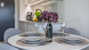 Una mesa de comedor dispuesta con platos, cubiertos y copas de vino, con un jarrón de flores moradas en el centro.