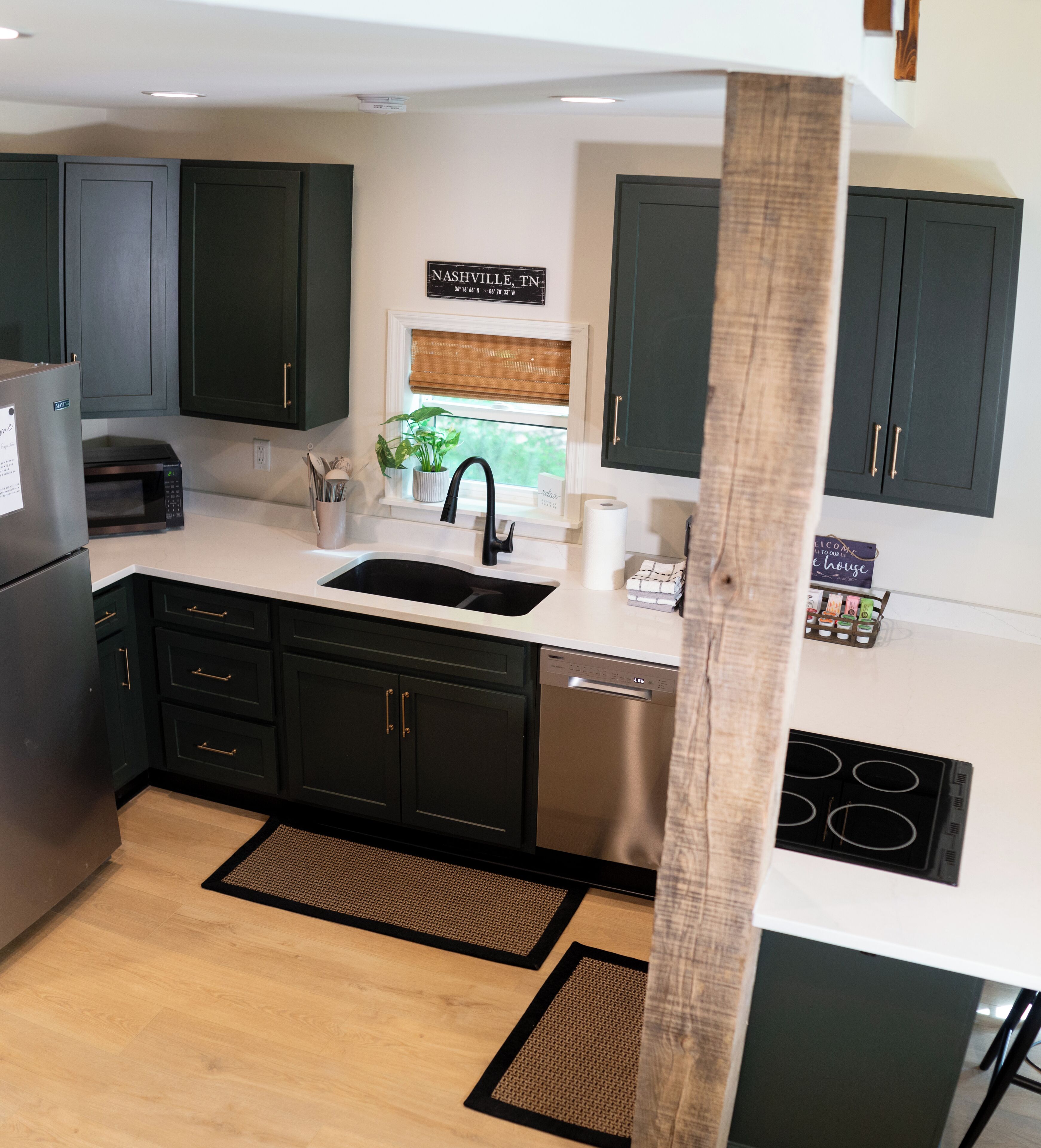 A modern kitchen with dark cabinets, a stainless steel refrigerator, a microwave, a sink, and a stove.