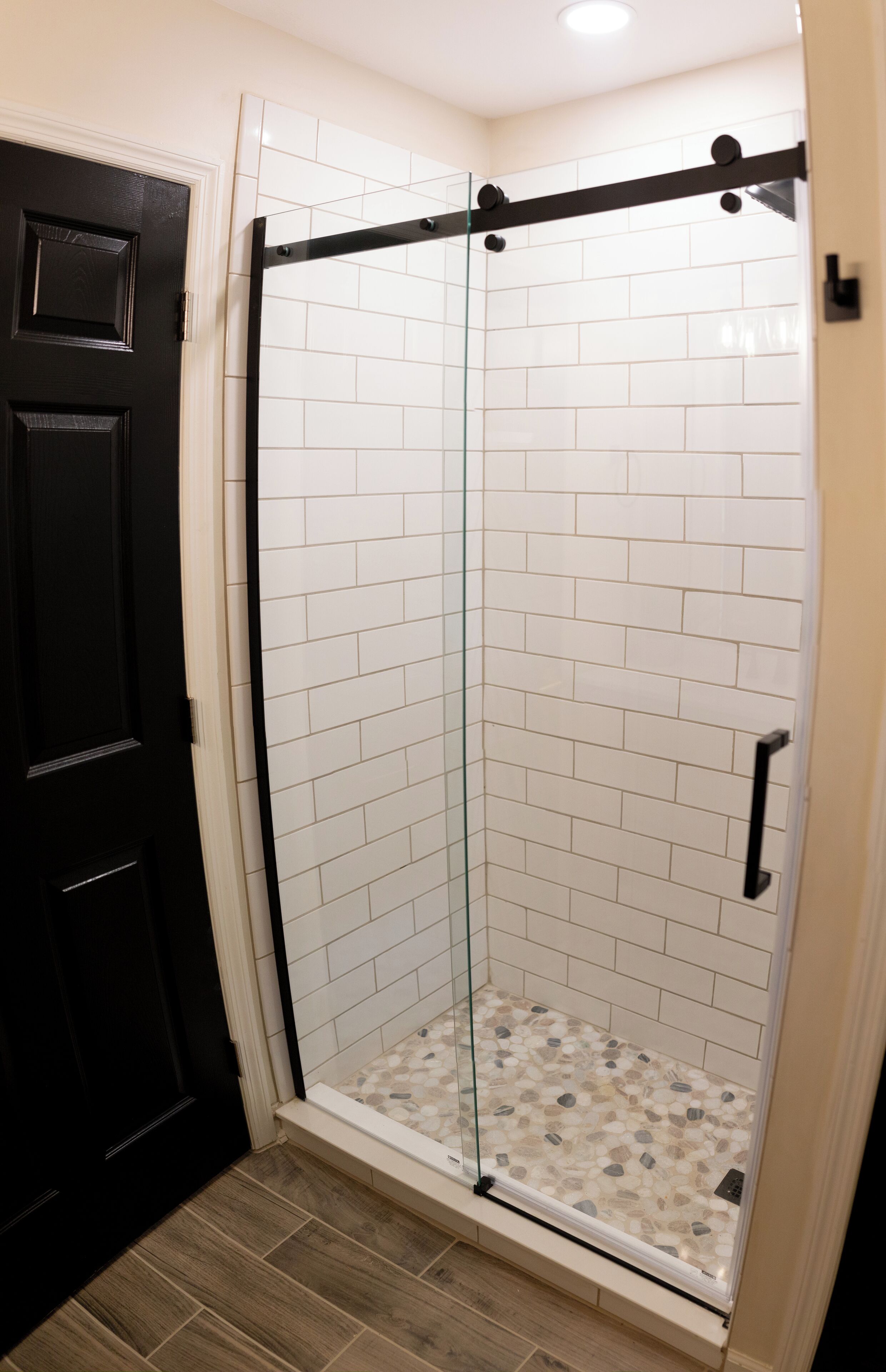 Une douche fermée par des parois de verre, avec des murs recouverts de carreaux blancs et un plancher en bois.