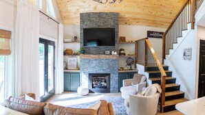 Una sala de estar moderna con chimenea, una escalera de madera y un televisor de pantalla plana montado en una pared de piedra.