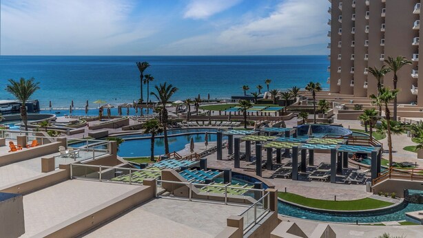 Et resort med flere swimmingpools, palmer og udsigt over havet.