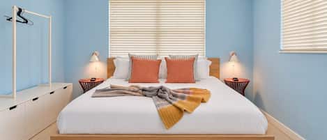 Una camera da letto con un letto, comodini, una lampada a sospensione e una finestra con persiane.