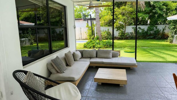 Um pátio moderno com um sofá modular, uma mesa de centro de madeira e uma cadeira de vime.