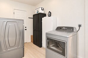 A laundry room with a front-loading washer and dryer, a tall black cabinet, and a white refrigerator. - Hot-Tub, Pool, Basketball, Fire Pit, Pong | Casa (Miami)